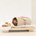 Baked goods wrapped in paper with a tag on a wooden stand, accompanied by a small bowl of nuts.