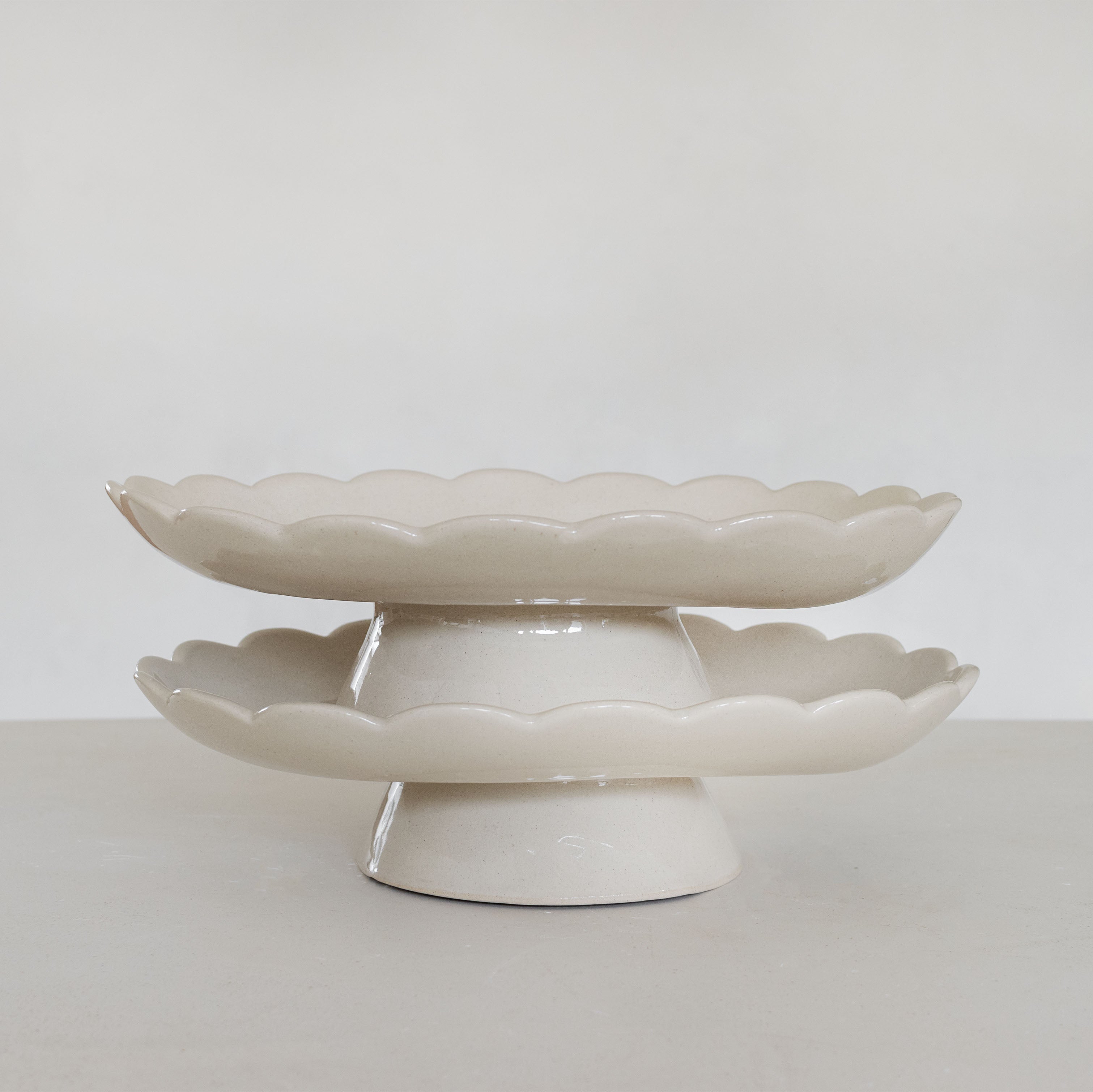 Two-tiered ceramic cake stand with scalloped edges on a plain background