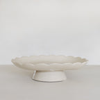 White ceramic cake stand on a light gray surface with a white background