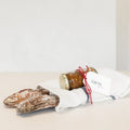 Two loaves of bread and a jar with a gift tag on a white surface.