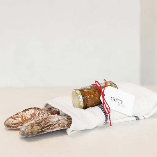 Two loaves of bread and a jar with a gift tag on a white surface.