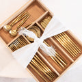 Set of gold cutlery in a wooden box with a white ribbon on a light background
