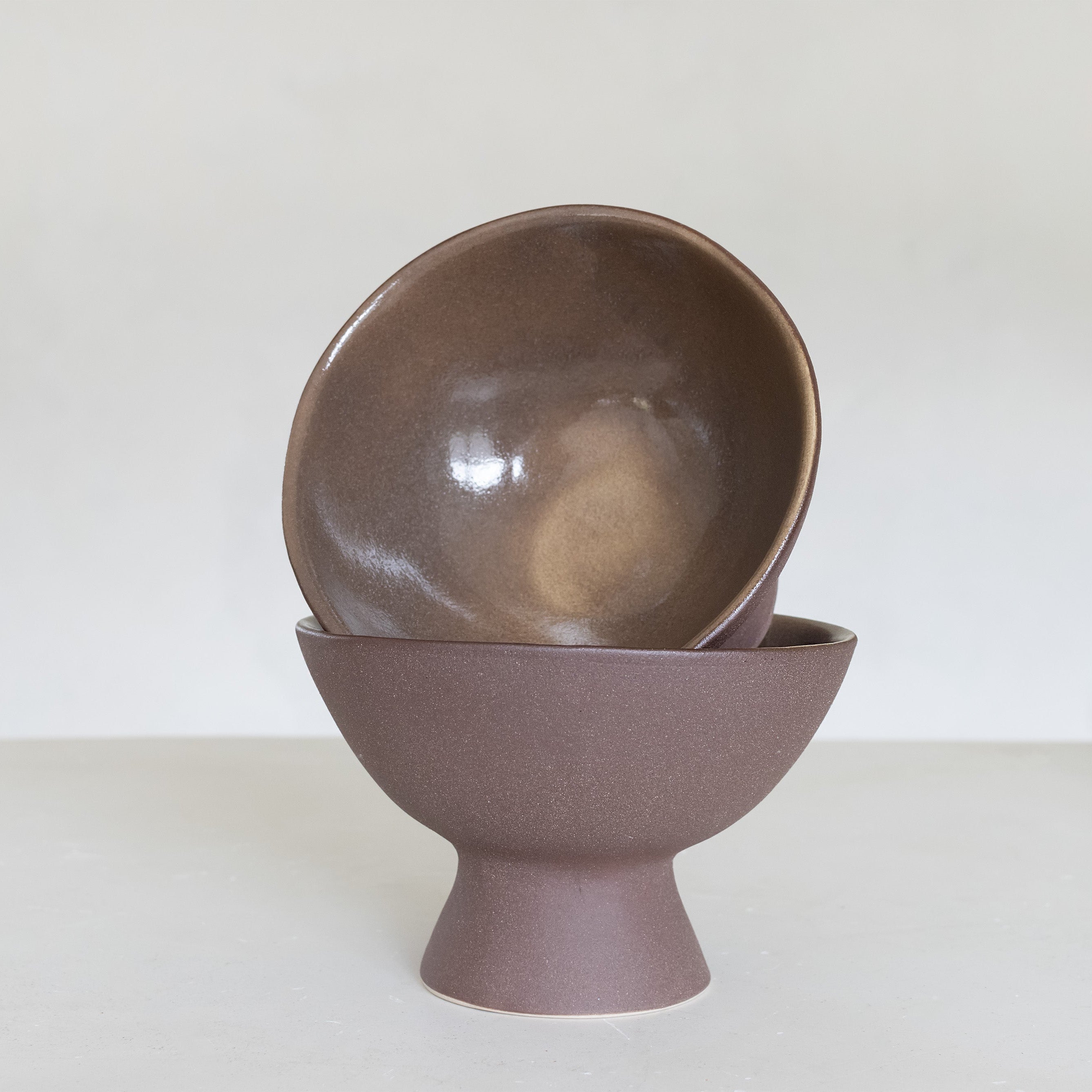 Brown ceramic bowl stacked on a matching stand against a white background