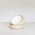 Two beige ceramic bowls stacked on a light surface with a white background