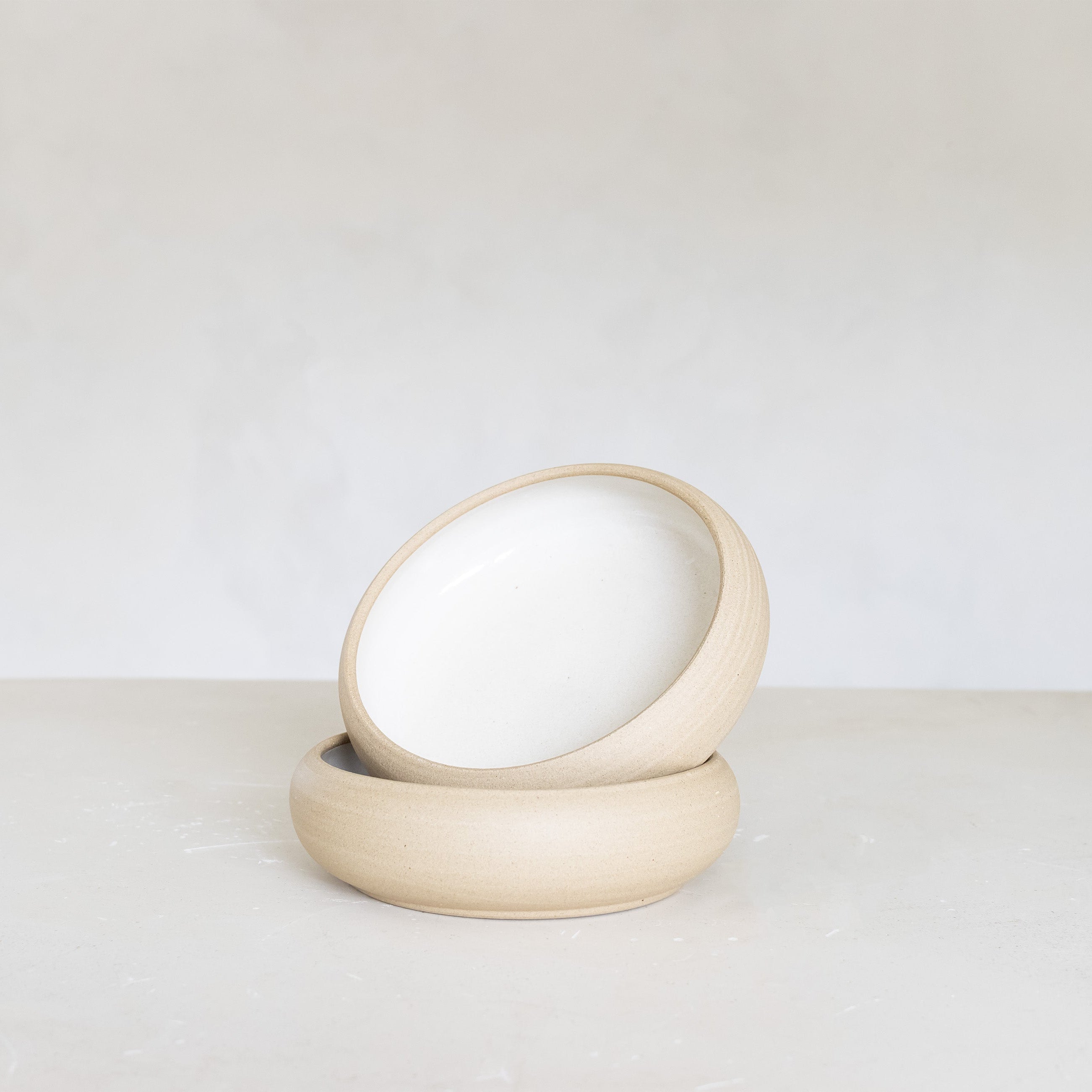 Two beige ceramic bowls stacked on a light surface with a white background