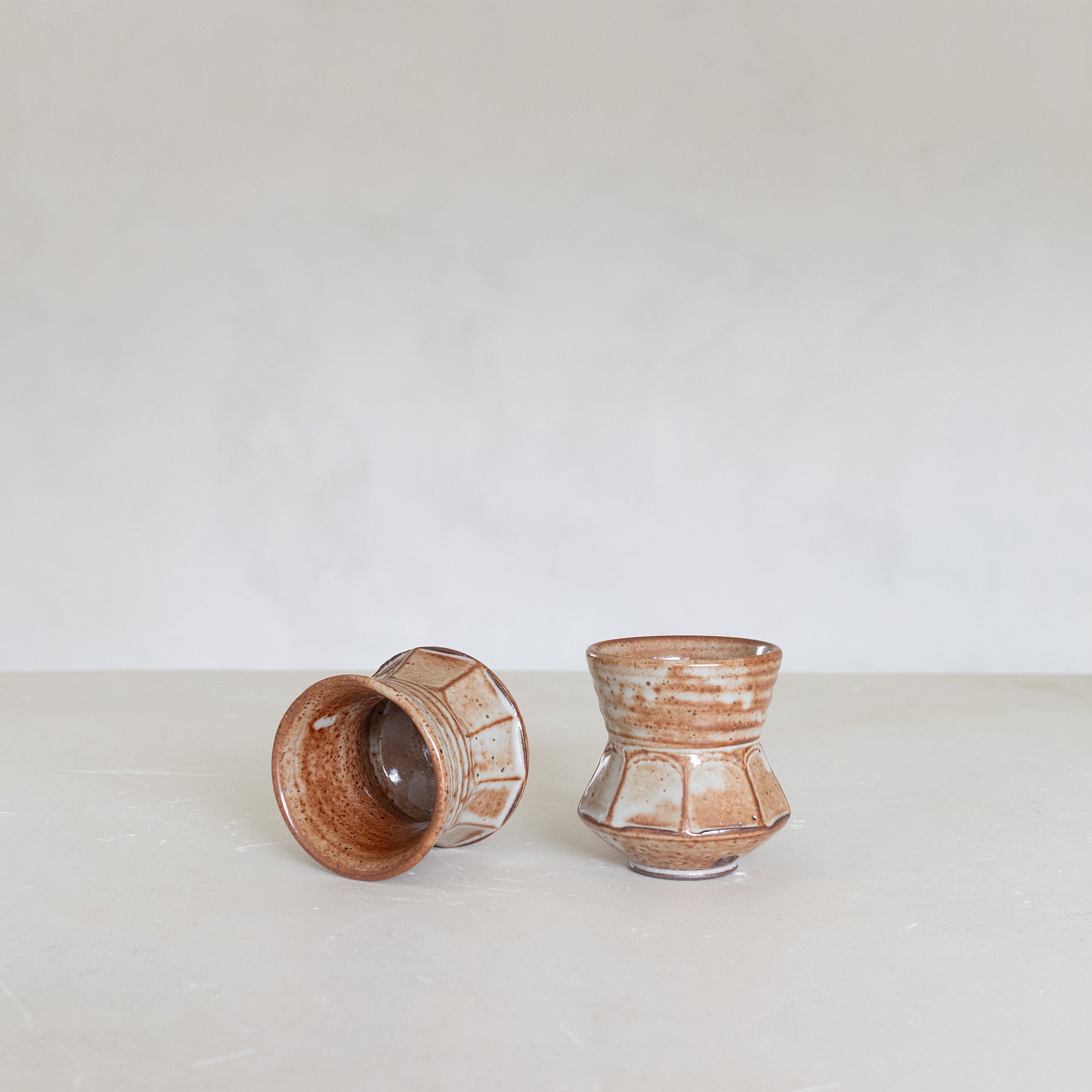 Two ceramic cups on a light surface with a white background