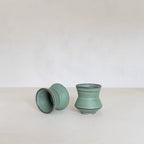 Two turquoise ceramic cups on a white surface with a light gray background