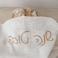 Loaf of bread wrapped in a white cloth with 'Artisan' embroidery on a neutral background