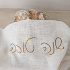 Loaf of bread wrapped in a white cloth with 'Artisan' embroidery on a neutral background