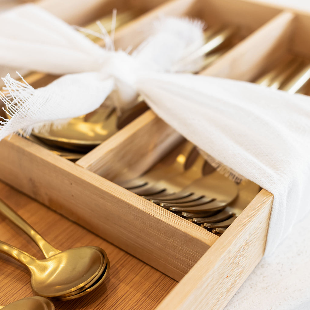 Gold cutlery set in a wooden drawer with white cloth
