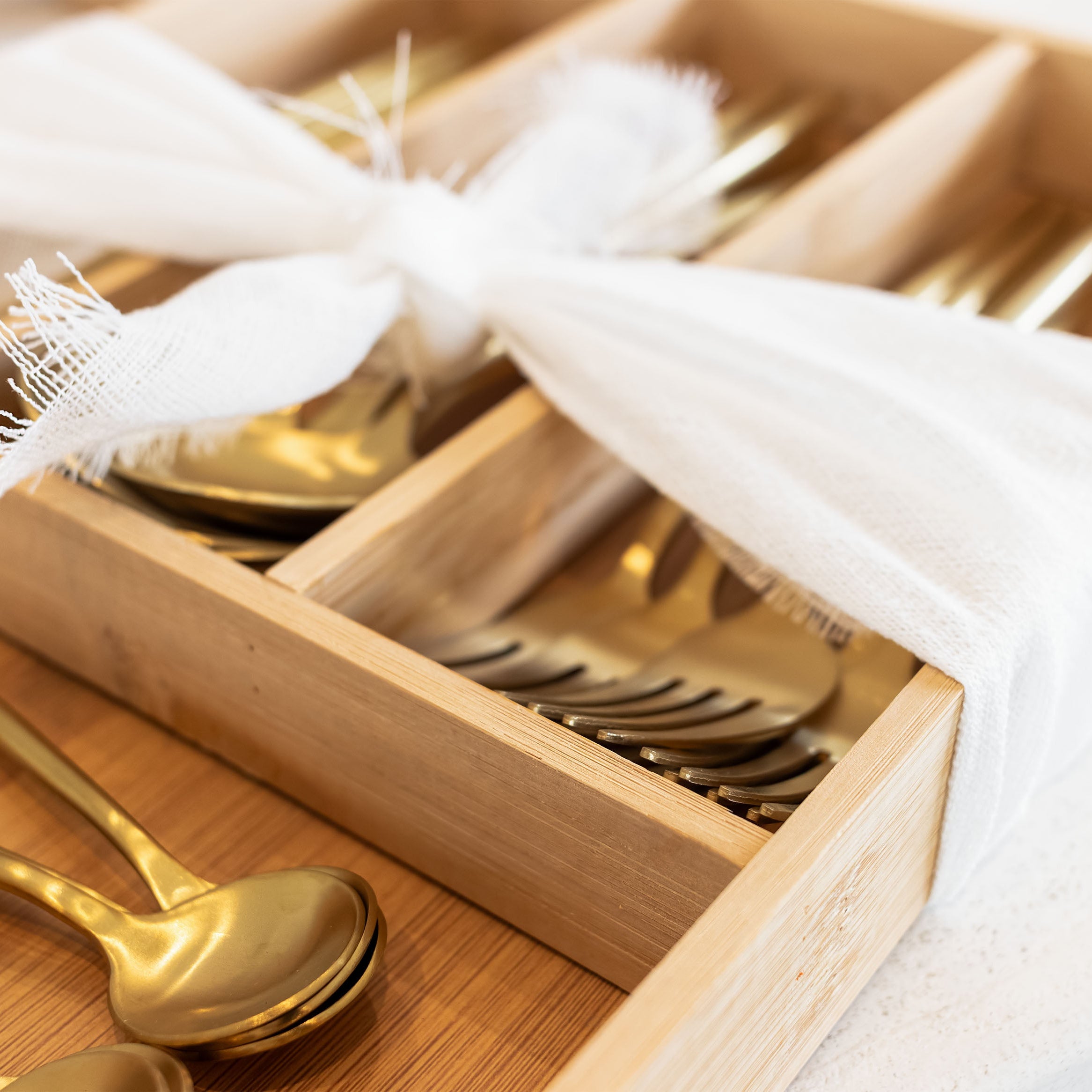 Gold cutlery set in a wooden drawer with white cloth