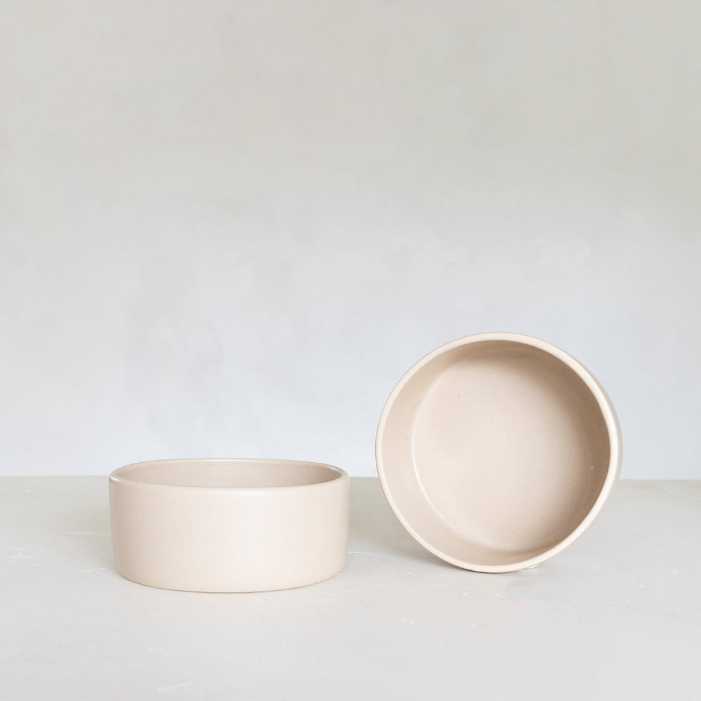 Two blush ceramic bowls on a light gray surface with a white background