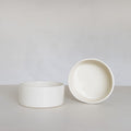 Two white ceramic bowls on a light gray surface with a plain background