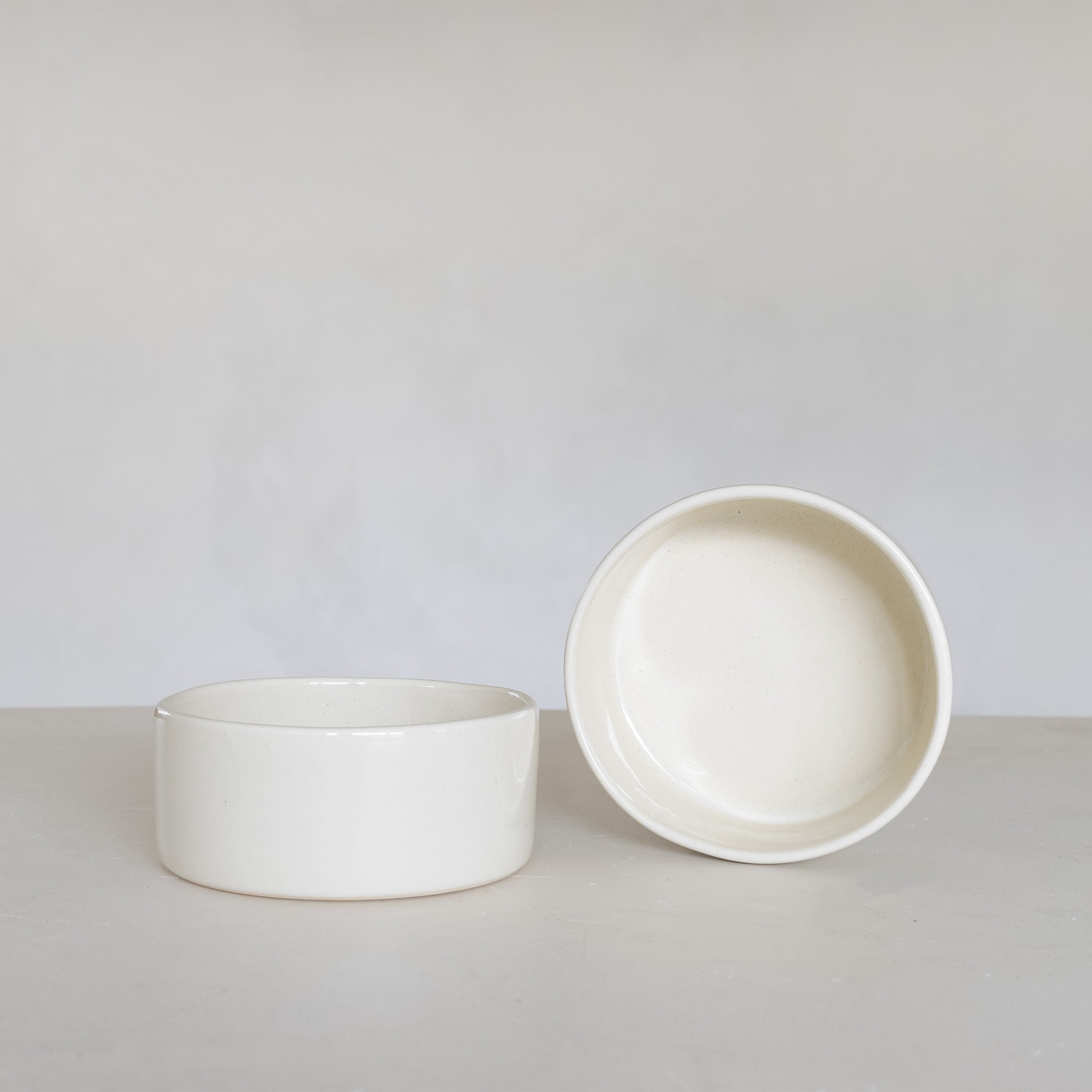 Two white ceramic bowls on a light gray surface with a plain background
