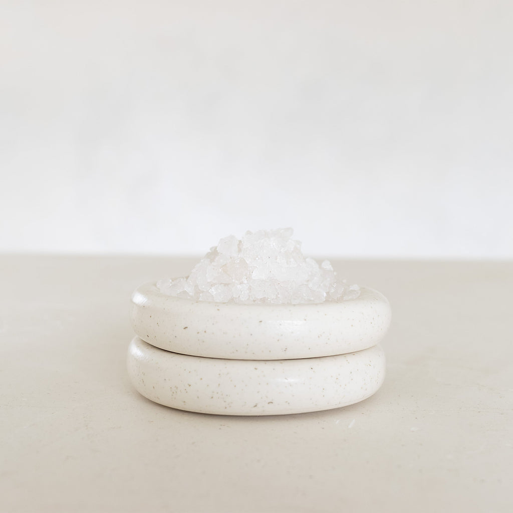 White ceramic jar with lid on a light beige surface with a white background