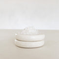 White ceramic jar with lid on a light beige surface with a white background