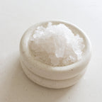 Small ceramic bowl filled with white sea salt on a light beige surface