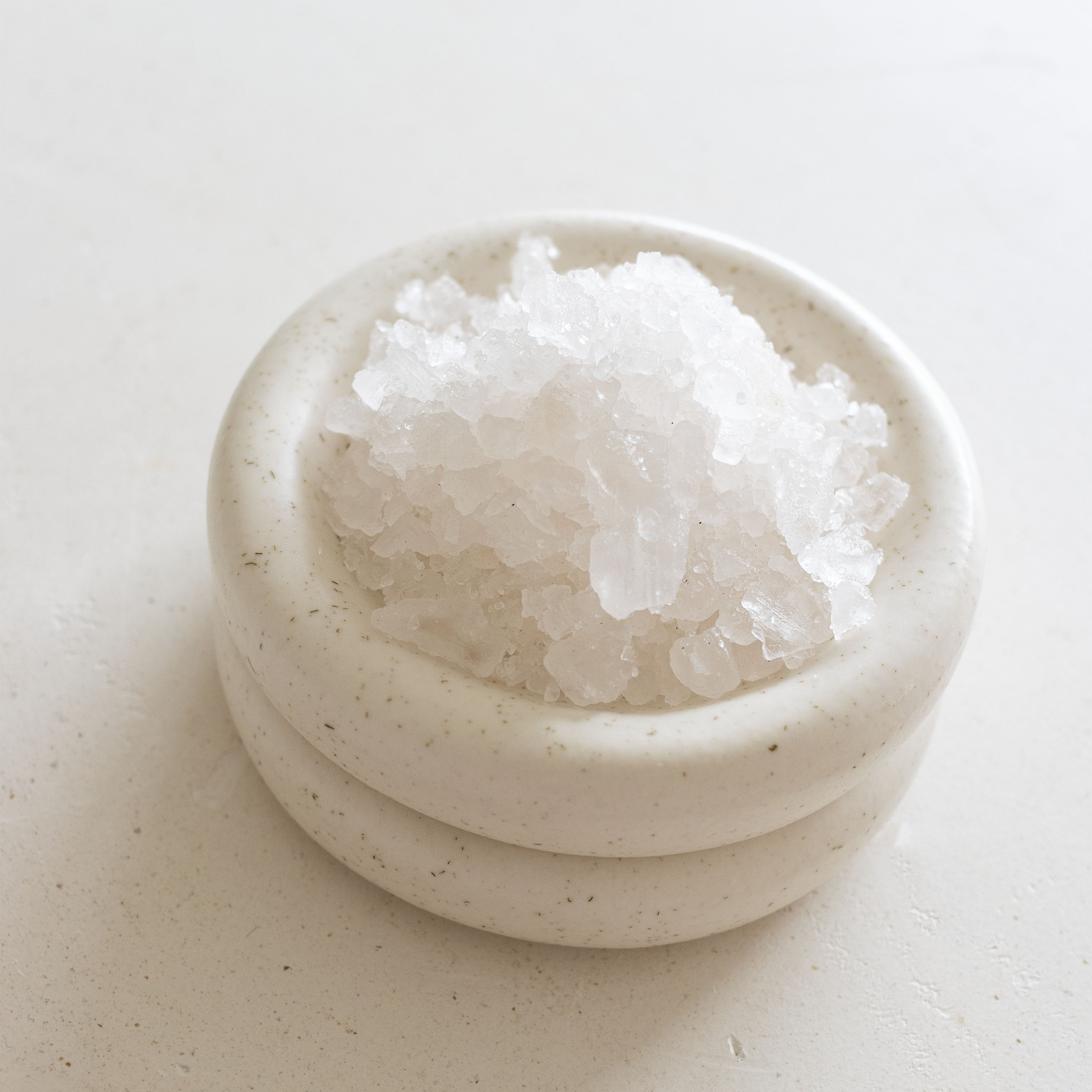Small ceramic bowl filled with white sea salt on a light beige surface