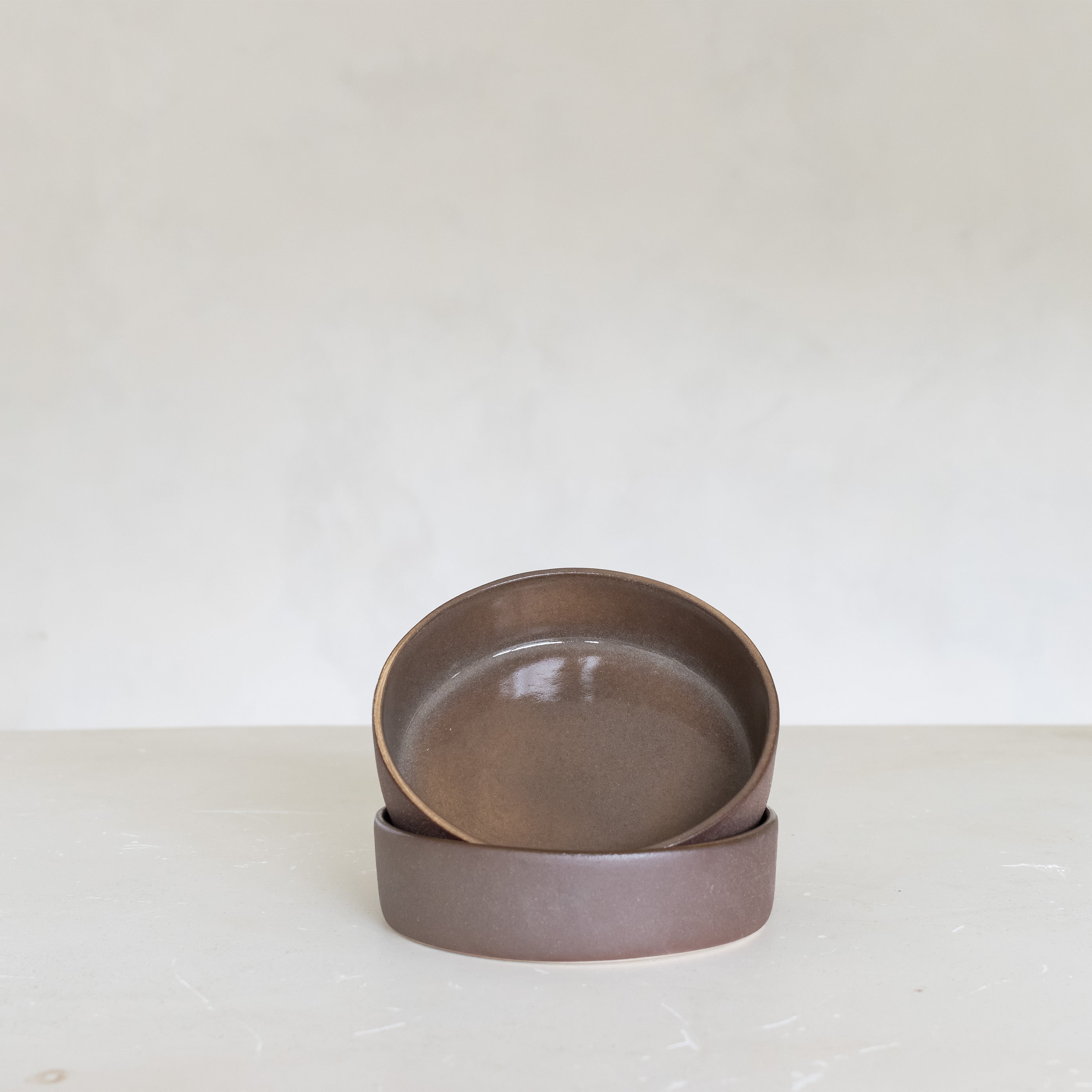 Two brown ceramic bowls stacked on a white surface with a white background