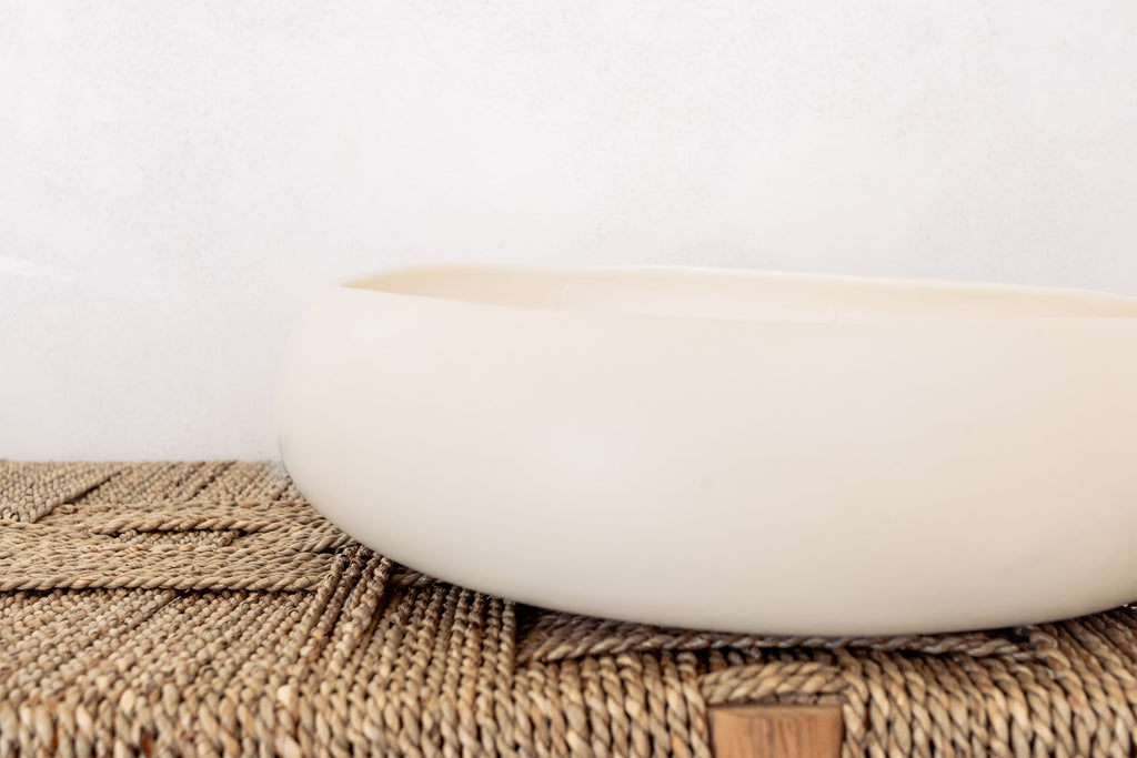 White ceramic candle on a woven bench with a white background