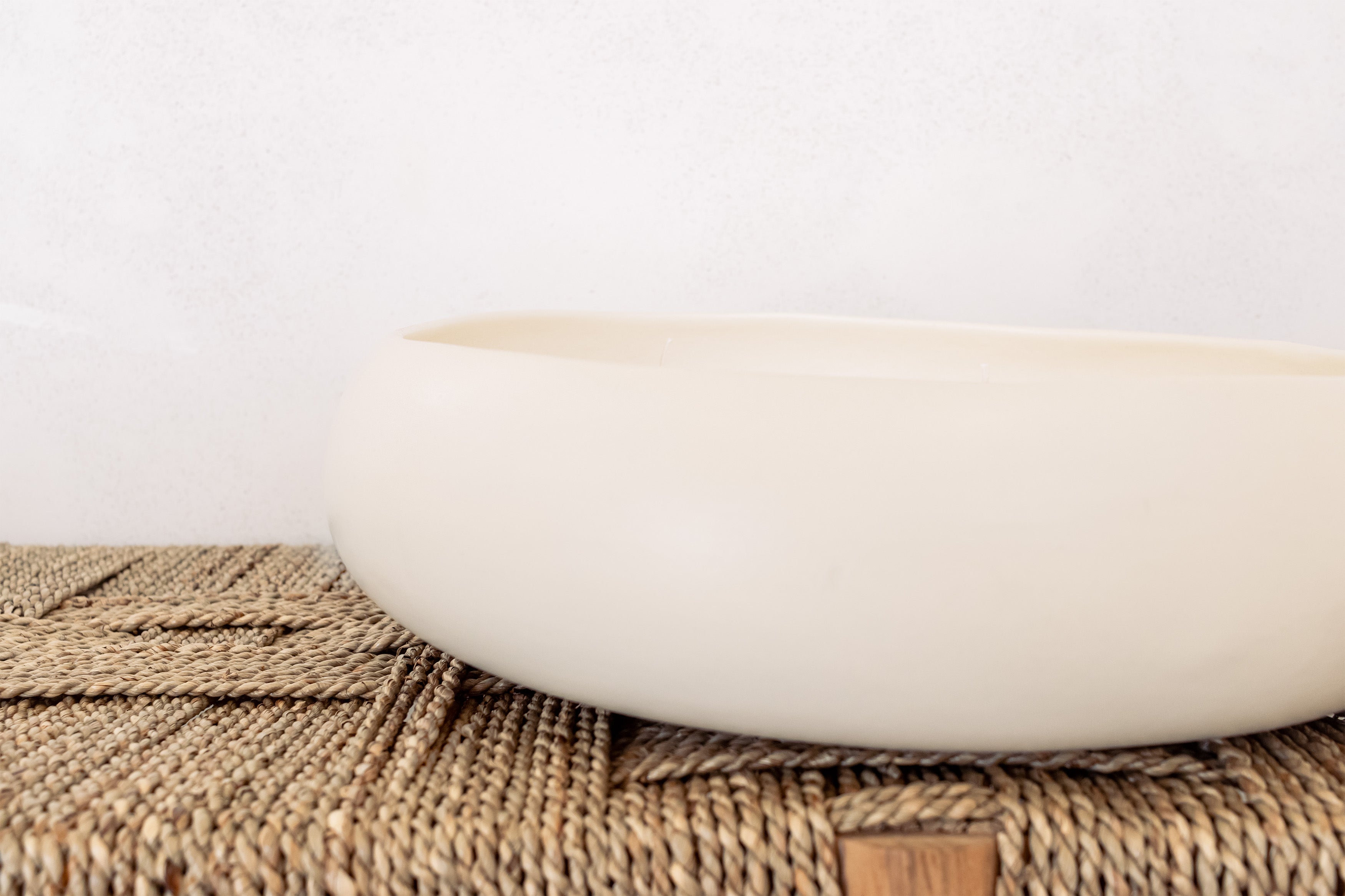 White ceramic candle on a woven bench with a white background