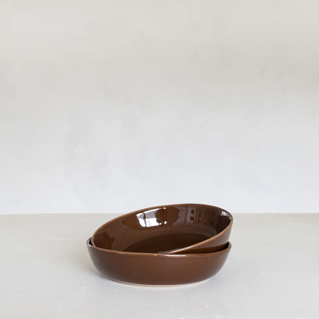 Two brown ceramic bowls stacked on a white surface with a white background