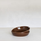 Two brown ceramic bowls stacked on a white surface with a white background
