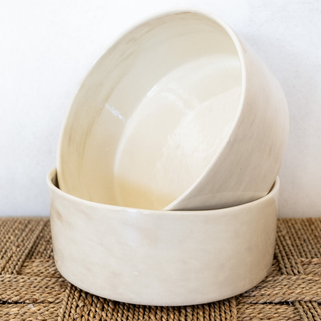 Two beige ceramic bowls stacked on a woven mat with a white background