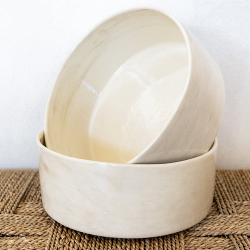 Two beige ceramic bowls stacked on a woven mat with a white background