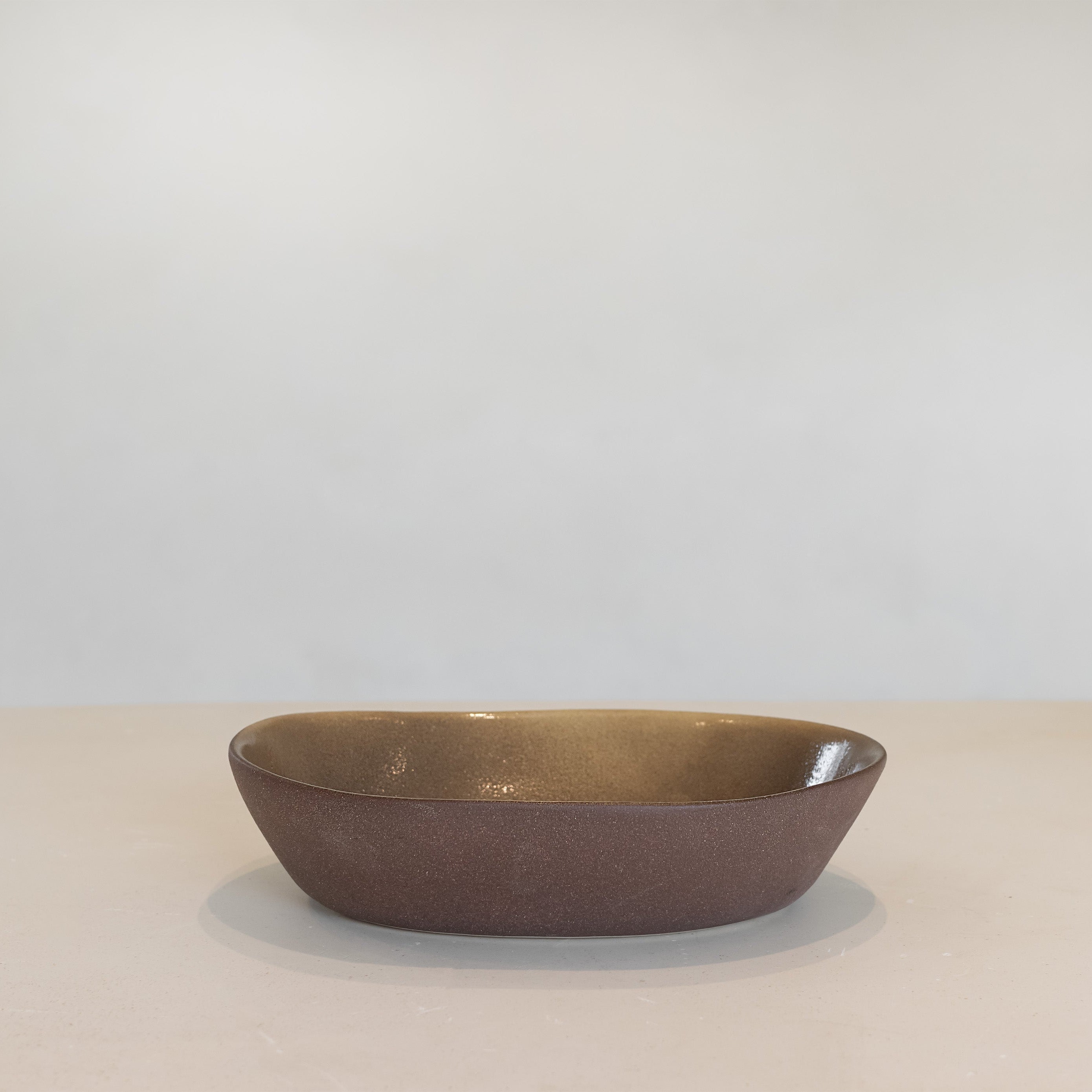 Brown ceramic bowl on a beige surface with a light gray background