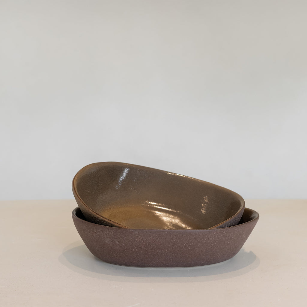 Two brown ceramic bowls stacked on a light surface with a white background