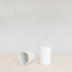 Two white ceramic beakers on a light beige surface with a light gray background