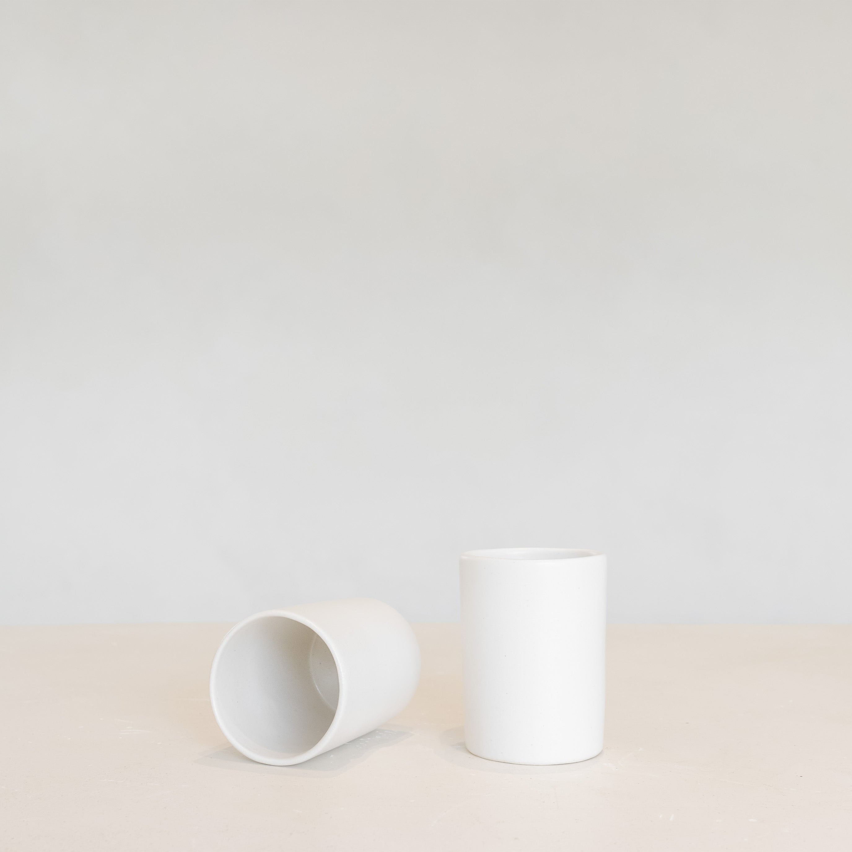 Two white ceramic beakers on a light beige surface with a light gray background