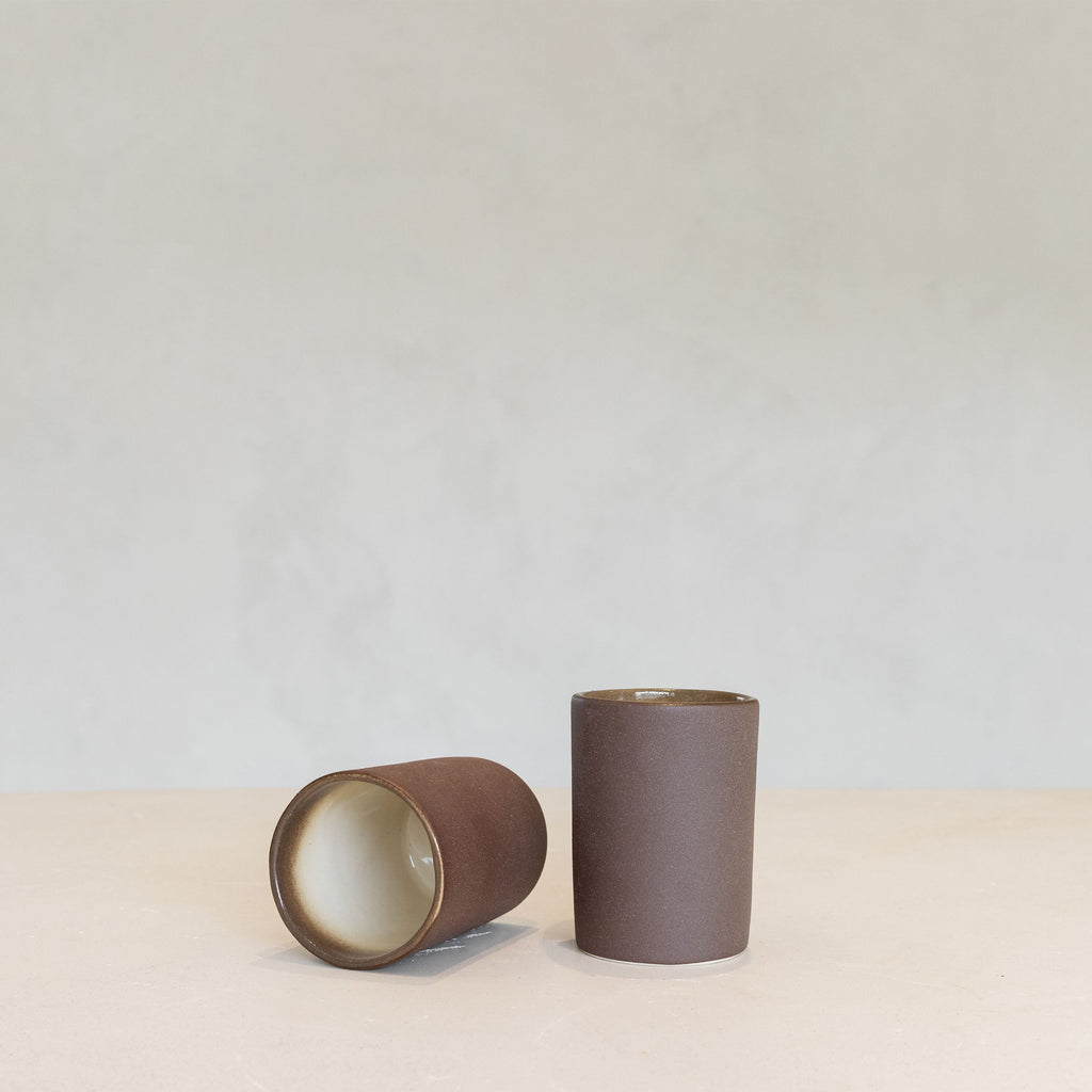 Two brown ceramic beakers on a light beige surface with a light gray background