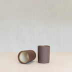 Two brown ceramic beakers on a light beige surface with a light gray background