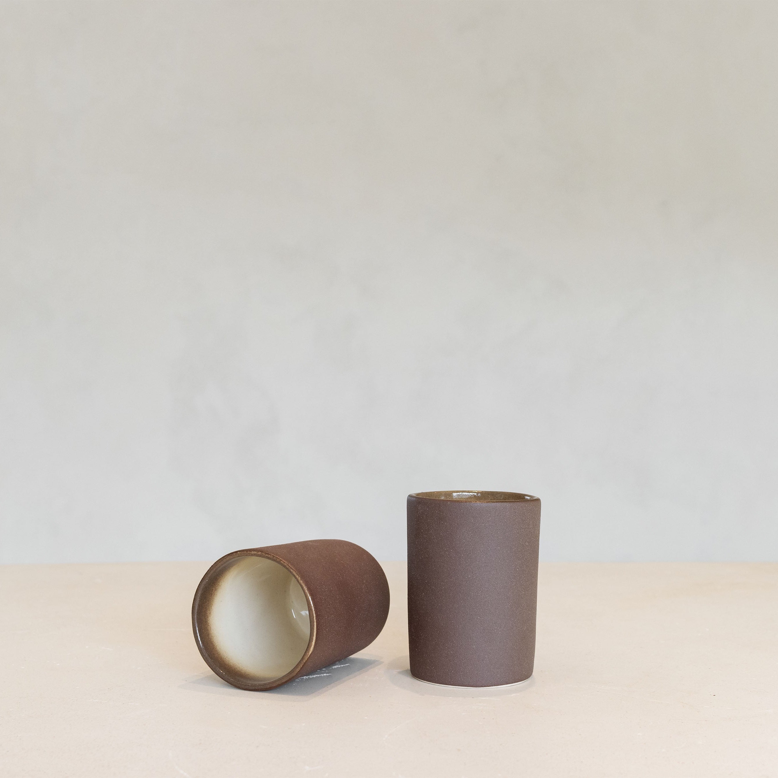 Two brown ceramic beakers on a light beige surface with a light gray background