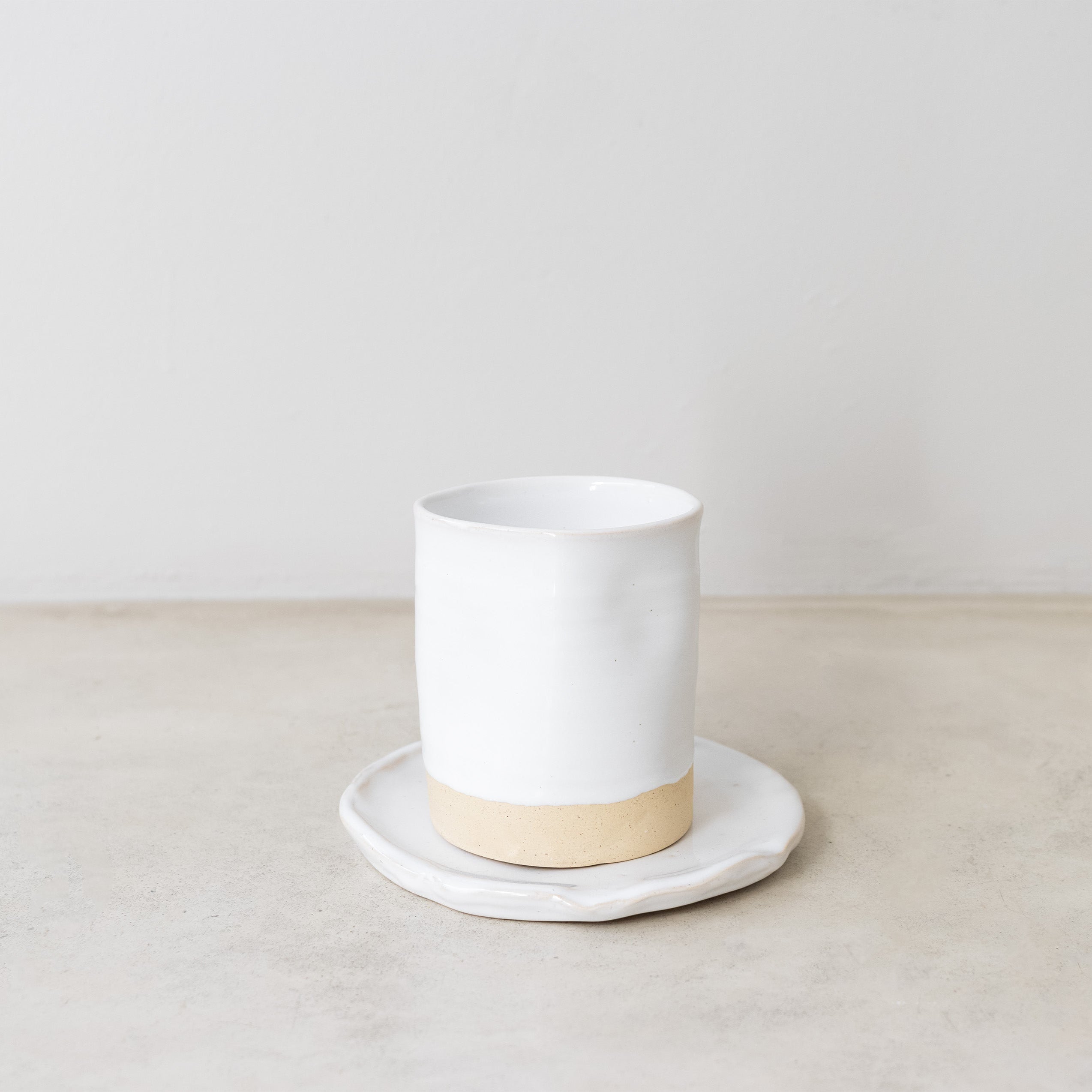 White ceramic cup with beige base on a white plate against a plain background