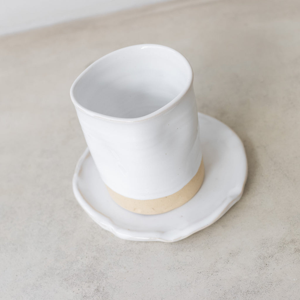 White ceramic cup with beige base on a matching saucer on a light gray surface