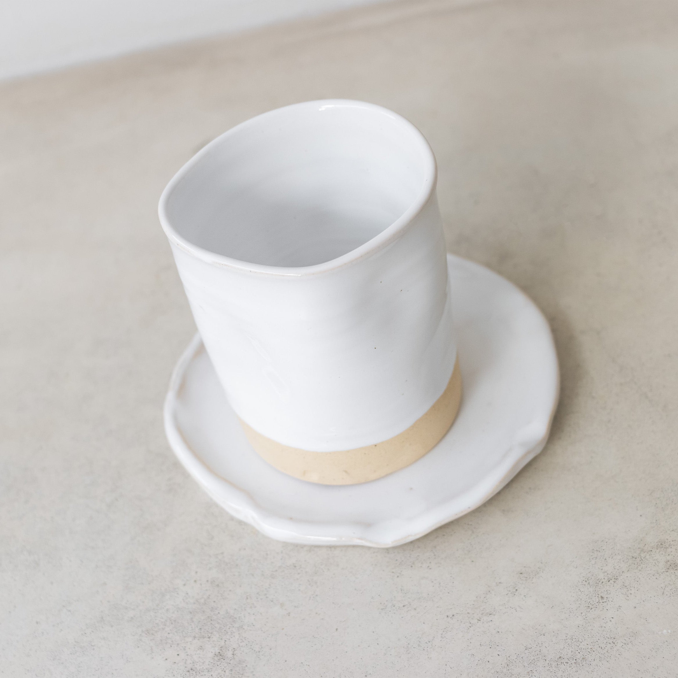 White ceramic cup with beige base on a matching saucer on a light gray surface